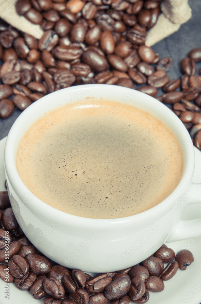 White cup of coffee and roasted fragrant dark coffee grains in bag White cup of coffee and roasted fragrant dark coffee grains in bag