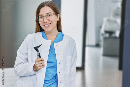 Portrait of female audiologist with otoscope standing in hearing clinic photo