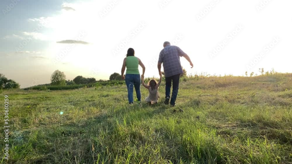 Rear view of family with one child spending time together outdoors. Father, mother holding hand in hand daughter, walking into sunset on meadow. Happy parents having leisure with kid at nature Rear view of family with one child spending time together outdoors. Father, mother holding hand in hand daughter, walking into sunset on meadow. Happy parents having leisure with kid at nature