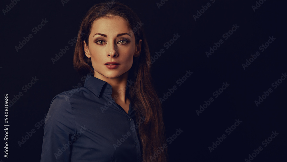Beautiful thinking serious business woman standing in blue shirt on black background with empty copy space for text. Closeup