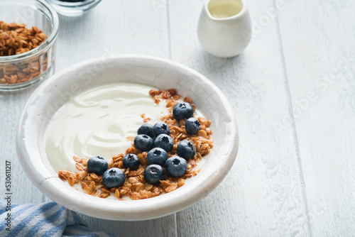 Yogurt. Greek Yogurt with granola and fresh blueberries in white bowl over old white wood background. Morning breakfast concept. Healthy food for breakfast, top view
