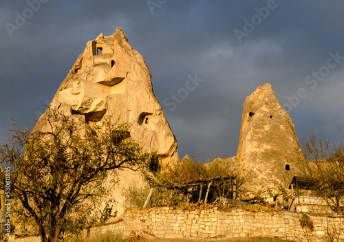 The view on partly collapsed natural rock formations and artificial caves, dovecotes inside it, known as fairy chimneys, located in Goreme, Cappadocia region, Turkey, illuminated by sun