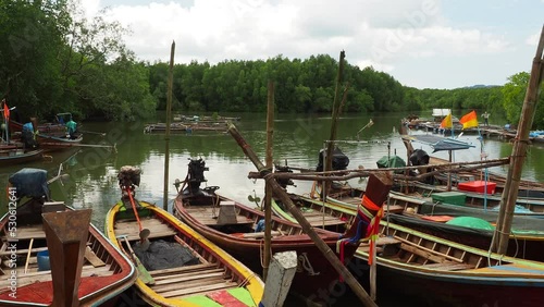 The scenery of docked small  fishing boats in the pier at Thung Wa district, Satun Province, Thailand, with floating bamboo baskets for keeping fish in water  and mangrove are in the background.  photo