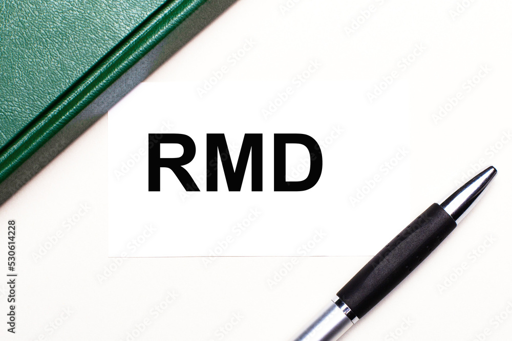 On a light gray background lies a pen, a green notebook and a white card with the text RMD Required Minimum Distributions. Business concept. On a light gray background lies a pen, a green notebook and a white card with the text RMD Required Minimum Distributions. Business concept.