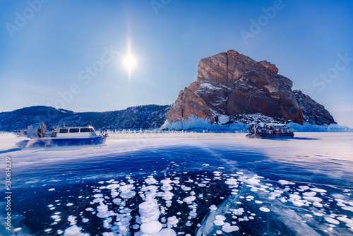Winter landscape sunny day blue clear ice on Baikal lake with hovercraft