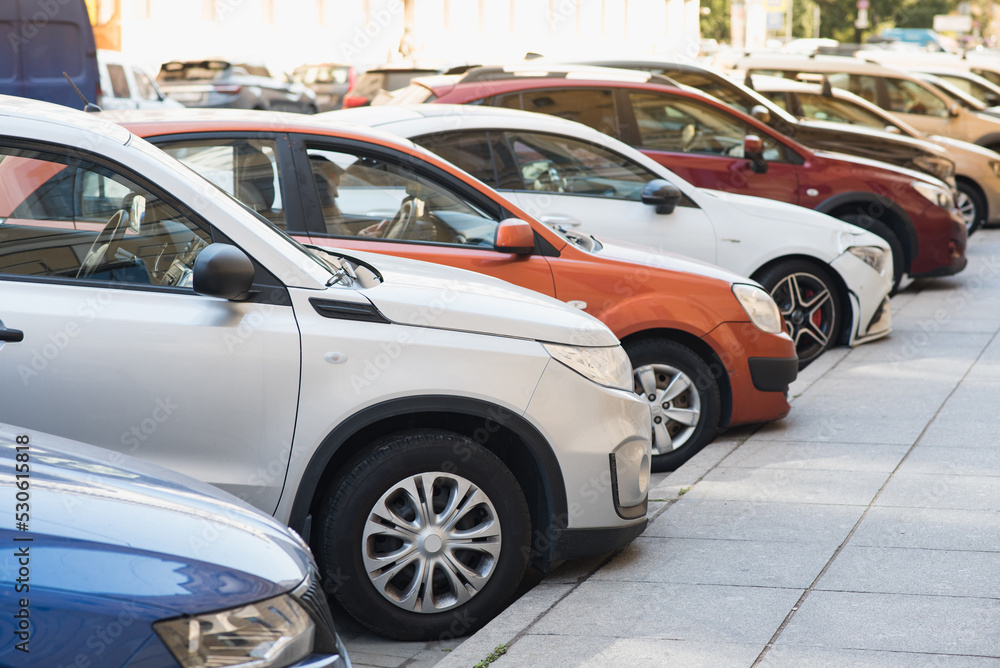 There are a lot of parked cars along the road in the city. Automobiles outside in the city.