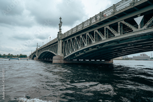 Fototapeta Naklejka Na Ścianę i Meble -  Bridge. A low metal bridge across the river in cloudy weather in gloomy dark colors. St. Petersburg