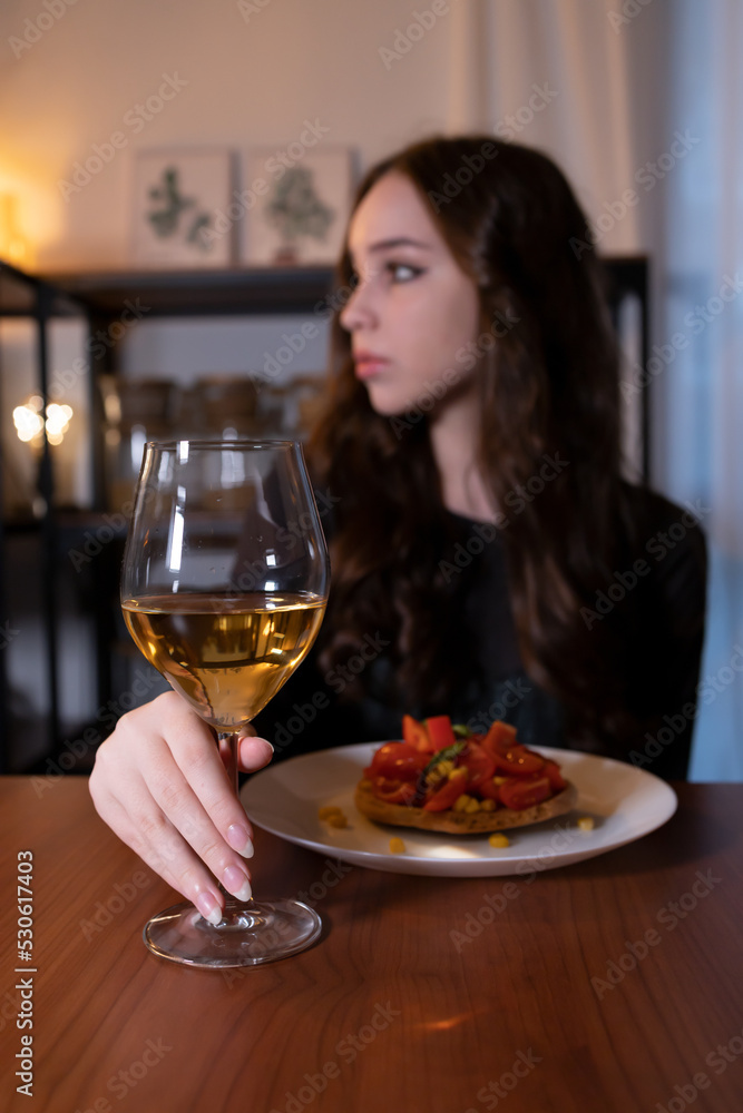 Young woman sitting in the kitchen with a glass of wine. Teen alcoholism concept, alcohol addiction problems among women Young woman sitting in the kitchen with a glass of wine. Teen alcoholism concept, alcohol addiction problems among women