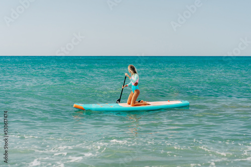 A young athletic woman is paddling on a paddleboard on the sea. © Ilona