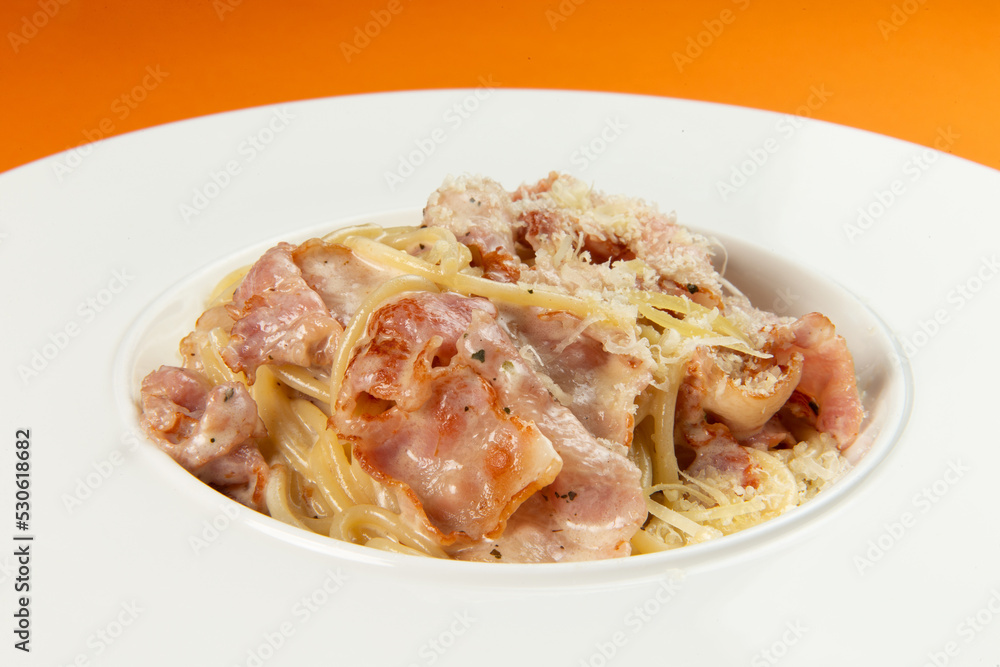 Pasta with bacon in a plate on an orange background. Pasta with bacon in a plate on an orange background.
