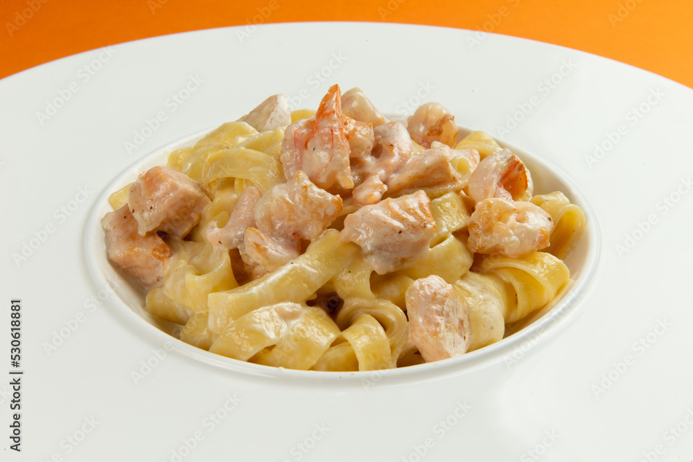 Pasta with salmon in a plate on an orange background.
