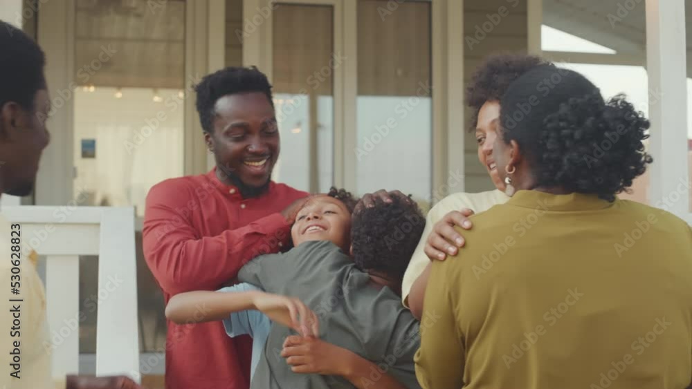 Medium shot of two happy African American couples with 11-12 year old kids meeting on front porch, greeting and hugging each other Medium shot of two happy African American couples with 11-12 year old kids meeting on front porch, greeting and hugging each other