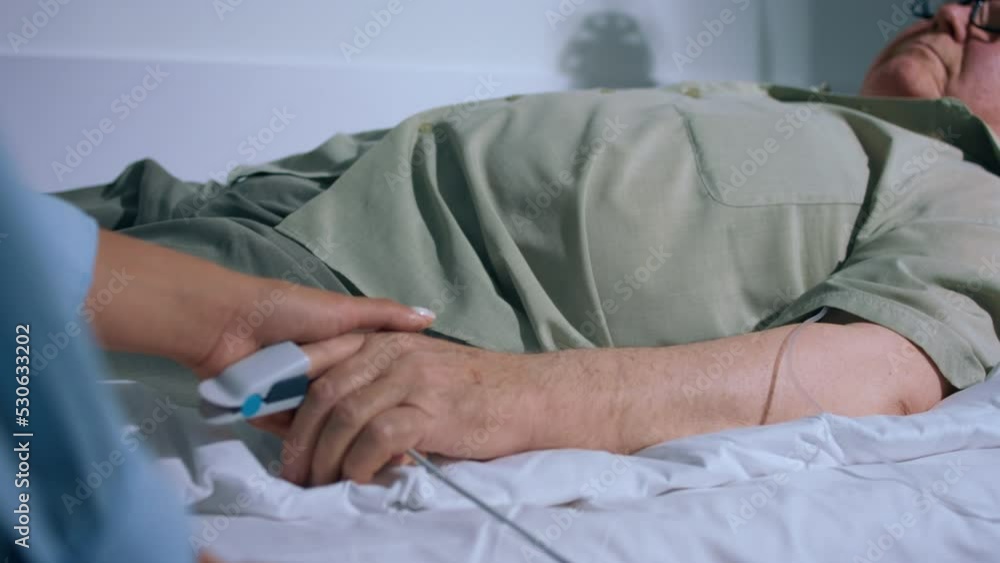 In the hospital room on the bed old man measure the heart rate monitor pulse oximeter showing pulse one of family member holding his hands and supporting him In the hospital room on the bed old man measure the heart rate monitor pulse oximeter showing pulse one of family member holding his hands and supporting him