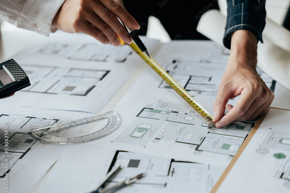 Close up of hands working brainstorming and measuring for cost estimating on paperworks and floor plan drawings about design architectural and engineering for houses and buildings.