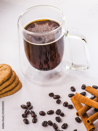 Glass thermal cup with coffee from a coffee machine on a white background. There are large coffee beans and a coffee machine next to the thermo mug. photo