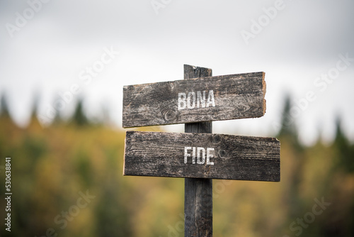 vintage and rustic wooden signpost with the weathered text quote bona fide, outdoors in nature. blurred out forest fall colors in the background.