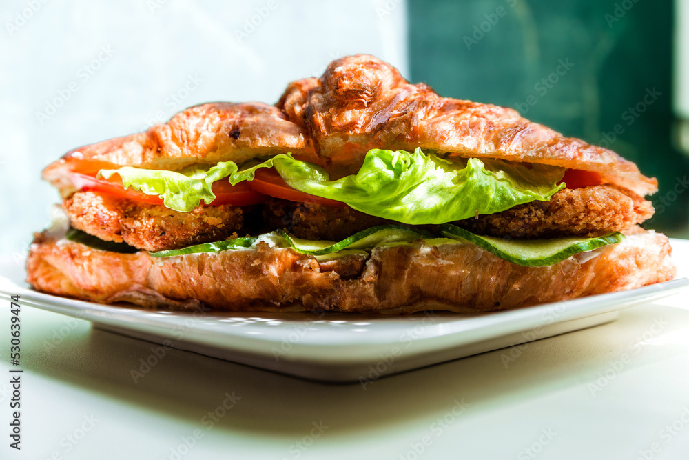 Croissant with chicken cutlet and fresh vegetables illuminated by sunlight. Croissant with chicken cutlet and fresh vegetables illuminated by sunlight.