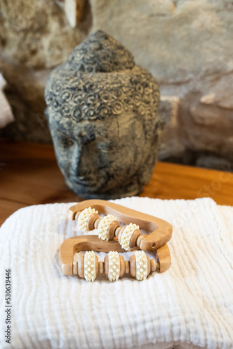 Detail of a wood therapy roller for massage. A Buddha sculpture in the background photo