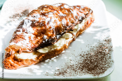 Croissant with chocolate spread and banana is illuminated by sunlight.