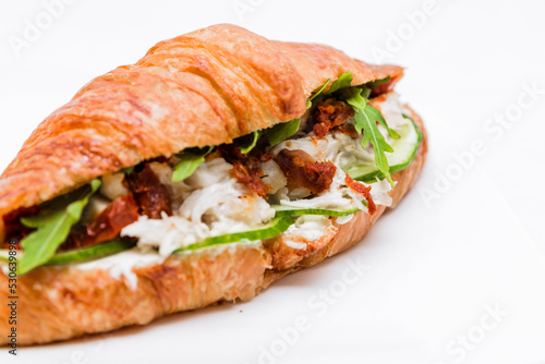 Croissant with squid meat, cheese, fresh cucumber, sun-dried tomato and lettuce arugula on a white background.