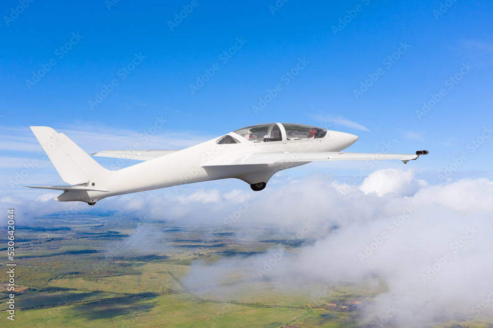 The glider is flying over the clouds and fields of the rural landscape.