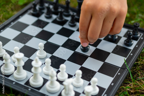Child playing chess on the lawn. Little boy makes first move and developing chess strategy, play board game with friend.