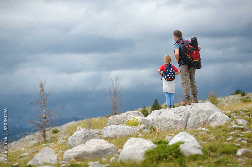 Cute schoolchild and mature father hiking together on mountain and exploring nature. Child learning survival skills and orienteering. Concepts of adventure, scouting and hiking tourism for kids.