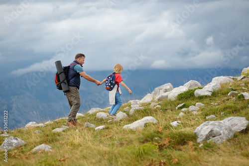 Cute schoolchild and his mature father hiking together on mountain and exploring nature. Concepts of adventure, scouting and hiking tourism for kids.
