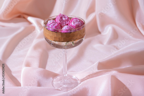 Bokal glass with roses in champagne on fabric folds background. Creative still life in pastel pink colors photo