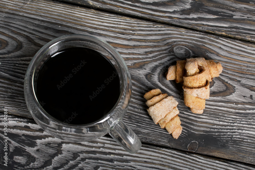 Croissants with cinnamon. Rolls with cinnamon. They lie on a saucer. There is a cup of coffee next to it. Background from black pine boards. Shot close-up. Croissants with cinnamon. Rolls with cinnamon. They lie on a saucer. There is a cup of coffee next to it. Background from black pine boards. Shot close-up.