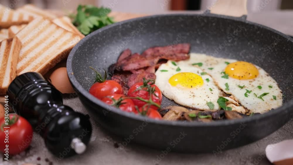 cooking tasty breakfast - fried bacon slices, eggs, mushrooms and tomatoes on a frying pan cooking tasty breakfast - fried bacon slices, eggs, mushrooms and tomatoes on a frying pan
