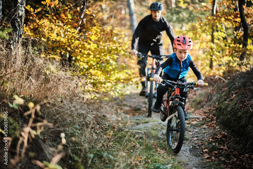 Fotografie Father and son mountain biking on path in woods