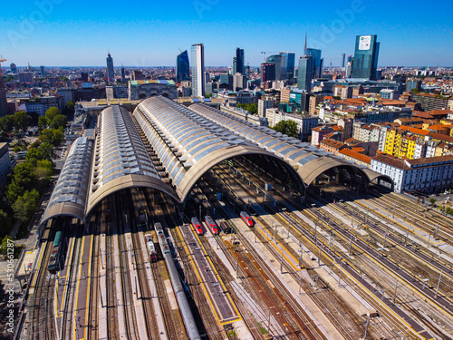 Aerial view of the station where trains arrive. An old arched structure made of metal and glass above the station poles. Tourism. Transport. Skyline with tall buildings. Italy, Milan, 09.2022