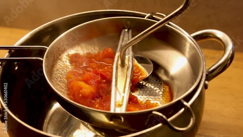 Przecieranie czerwonych pomidorów przez metalowe sito photo