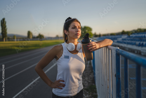 One woman stand at stadium with supplement water bottle take a brake