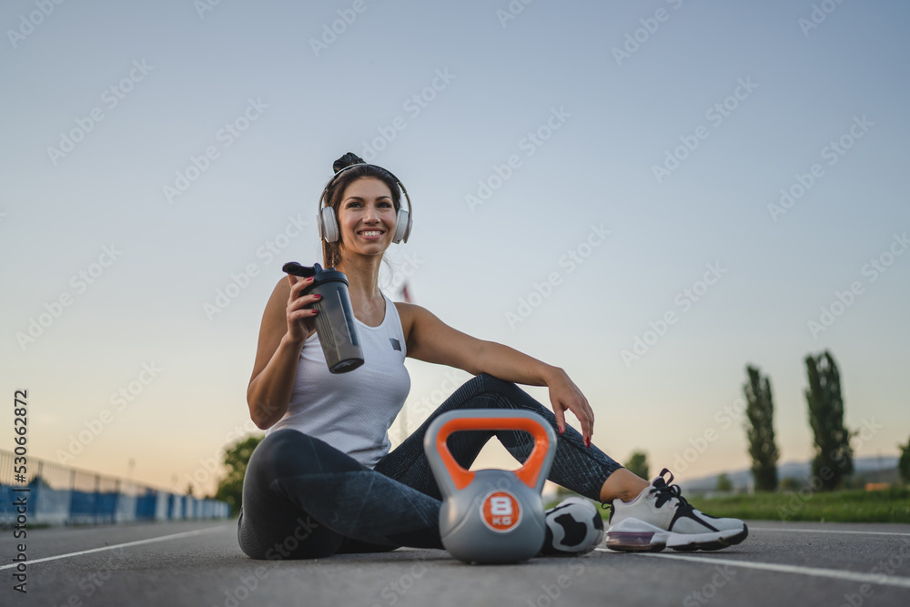 one caucasian woman female athlete rest hold supplement shaker kettlebell girya weight while sitting in stadium on track during training in summer evening copy space health and fitness concept one caucasian woman female athlete rest hold supplement shaker kettlebell girya weight while sitting in stadium on track during training in summer evening copy space health and fitness concept