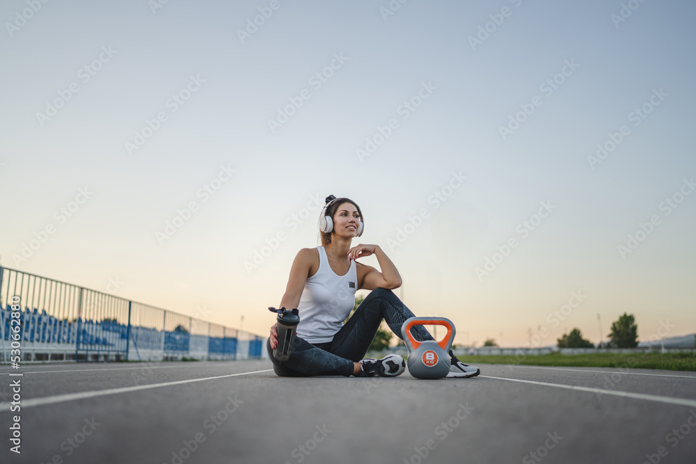 one caucasian woman female athlete rest hold supplement shaker kettlebell girya weight while sitting in stadium on track during training in summer evening copy space health and fitness concept one caucasian woman female athlete rest hold supplement shaker kettlebell girya weight while sitting in stadium on track during training in summer evening copy space health and fitness concept