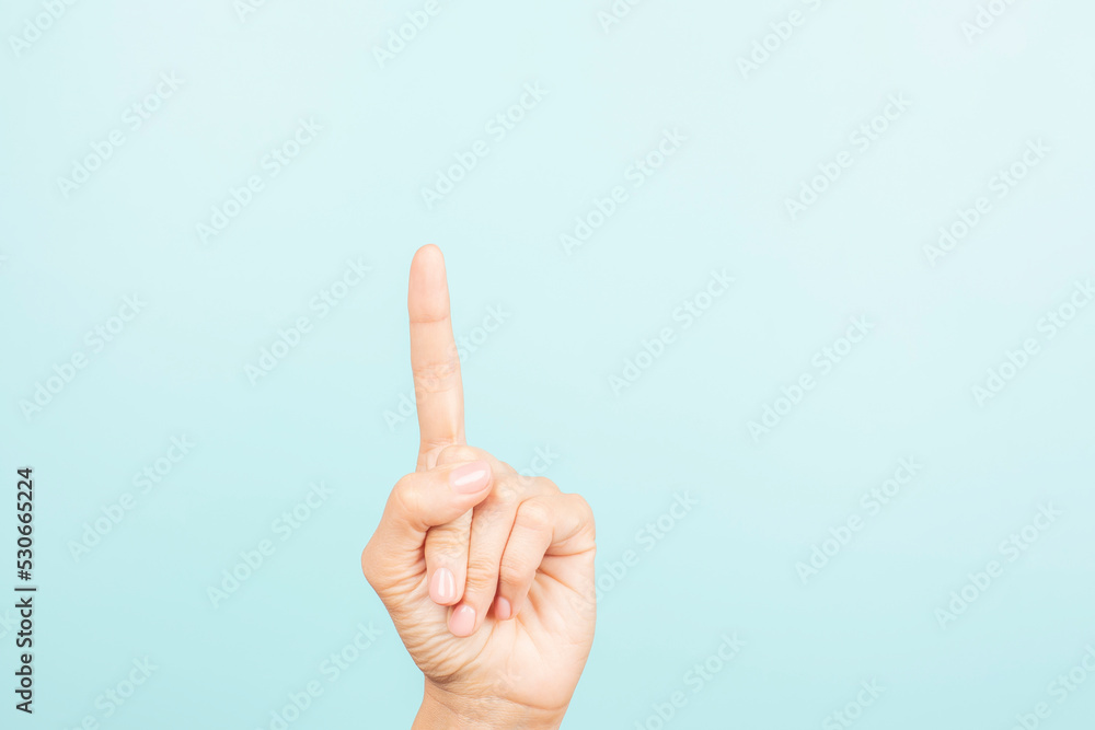 Female hand shows number one. Woman pointing up with index finger on light blue background