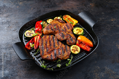 Traditionelles Barbecue Halsgrat vom Schwein mit gegrilltem Gemüse und Gewürzen als close-up in einer rustikalen Design Pfanne