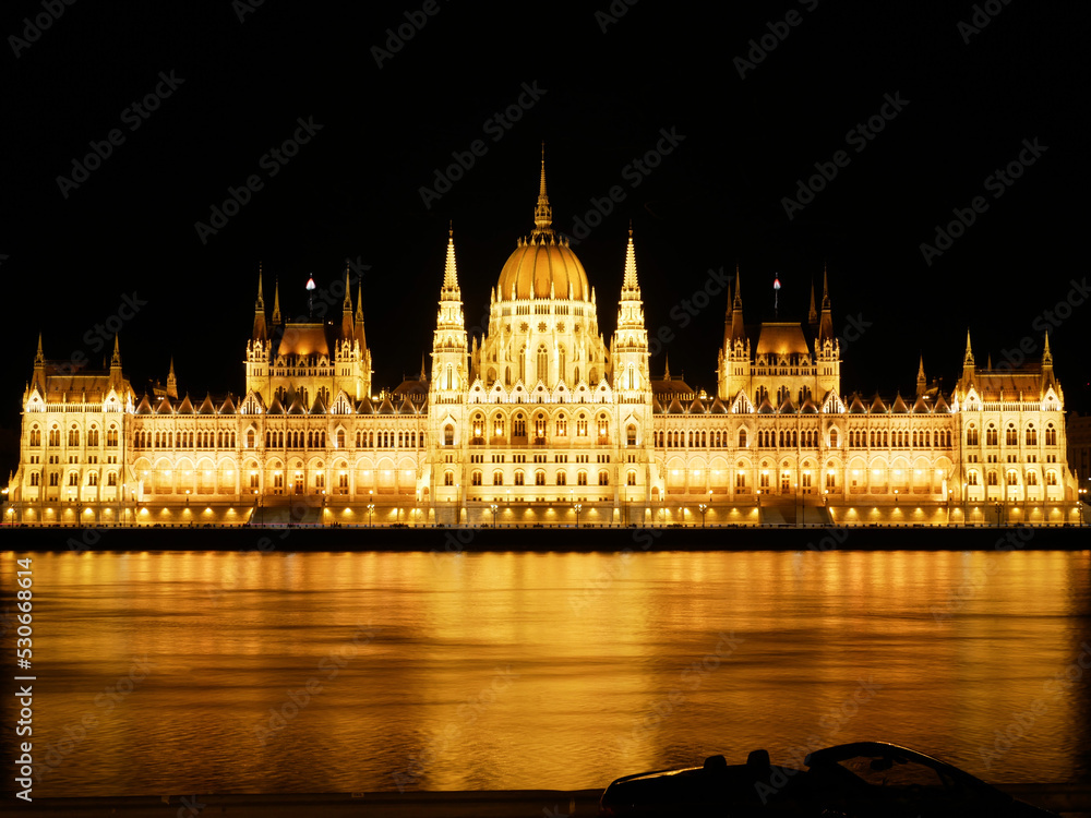 Budapest, Hungary - June 26 2022: Parliament building, Országház, parliament of Hungary. Night view over the calm Danube, as the parliament building is lit up in yellow colours under the black sky