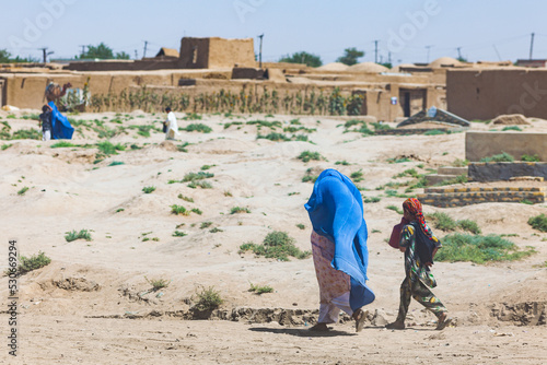 Woman wearing blue burka and daughter with a colourfull scarf walking in a poor afghan village near Andkhoy, Faryab Province, Northern Afghanistan