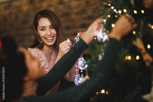 Female Friends Decorating Christmas Tree And Enjoying Holiday Time At Home