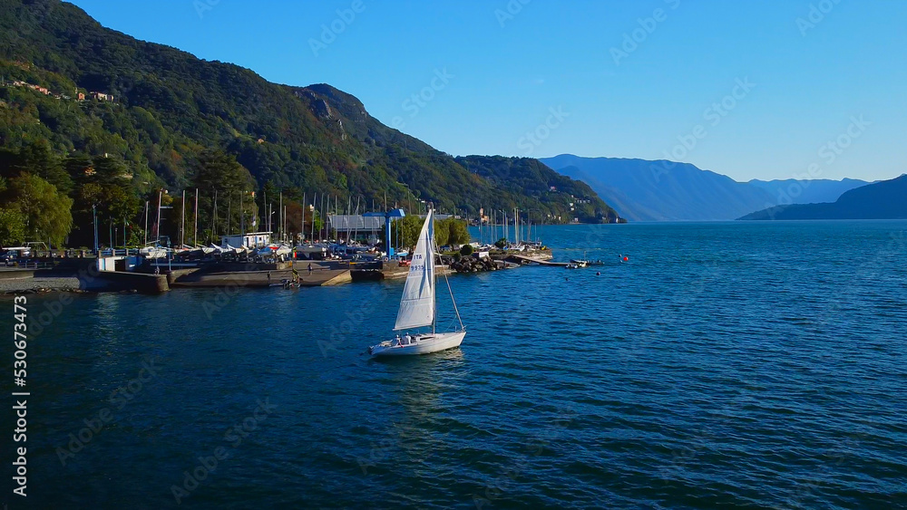Aerial view of a yacht with a white sail on Lake Como. Vacation in italy in the alps. Tourism and romance on a sailboat. Mountains around the lake. Sunny day. Green Planet. Italy, Bellano, 09.2022