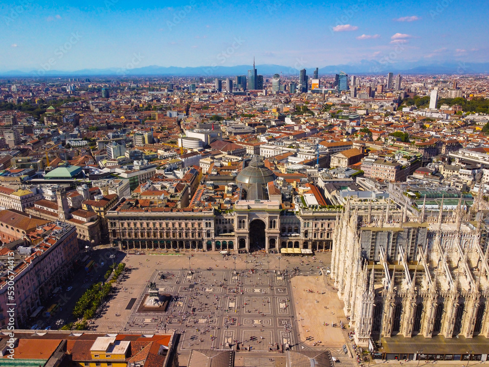 Fototapeta premium Aerial view of Piazza Duomo in front of the Gothic cathedral in the center. Drone view of the gallery and rooftops during the day. Flight over the city. People in the city. Milan. Italy 2022