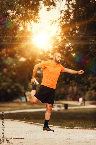 Happy positive sportsman during outdoor workout, man wearing sports outfit warming up muscles,enjoying active lifestyle outside in park © Minet