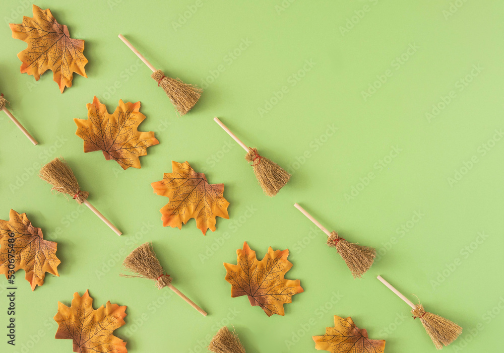 A pattern made of fall leaves and small brooms against pastel green background covering half of the picture. Empty copy space. Top view. Creative concept for Halloween or autumn web banner A pattern made of fall leaves and small brooms against pastel green background covering half of the picture. Empty copy space. Top view. Creative concept for Halloween or autumn web banner