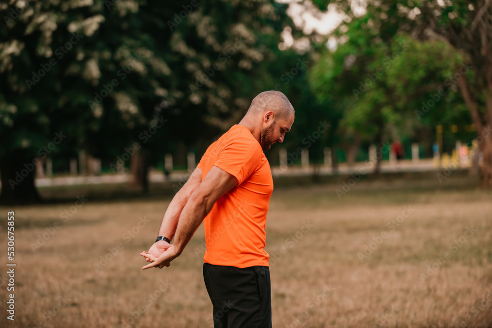 Happy positive sportsman during outdoor workout, man wearing sports outfit warming up muscles,enjoying active lifestyle outside in park Happy positive sportsman during outdoor workout, man wearing sports outfit warming up muscles,enjoying active lifestyle outside in park