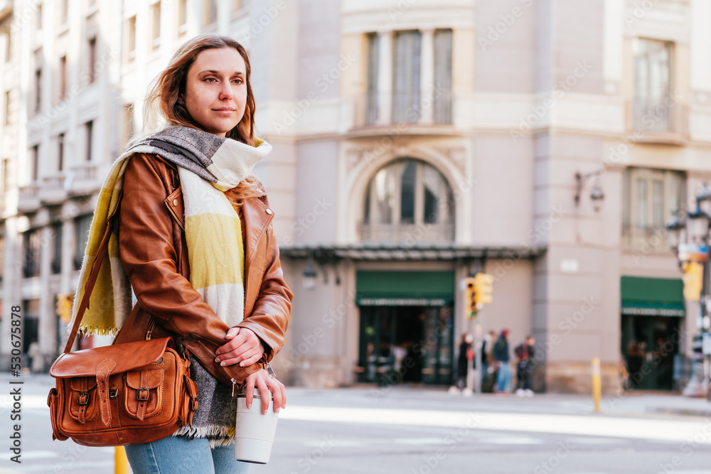 Fototapeta premium horizontal portrait of a trendy blonde woman waiting public transportation in the street. She holds a reusable coffee mug