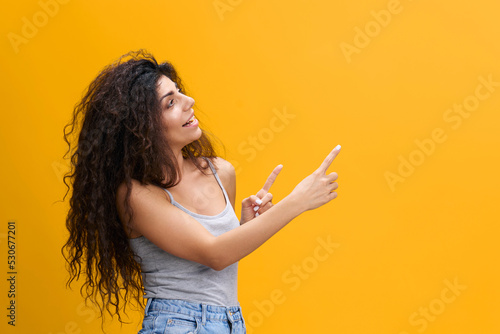 COOL OFFER. Happy beautiful sunburned Latin female with afro look up, point fingers up, show empty space, stay isolated over yellow background. Copy space, free place, mockup for design