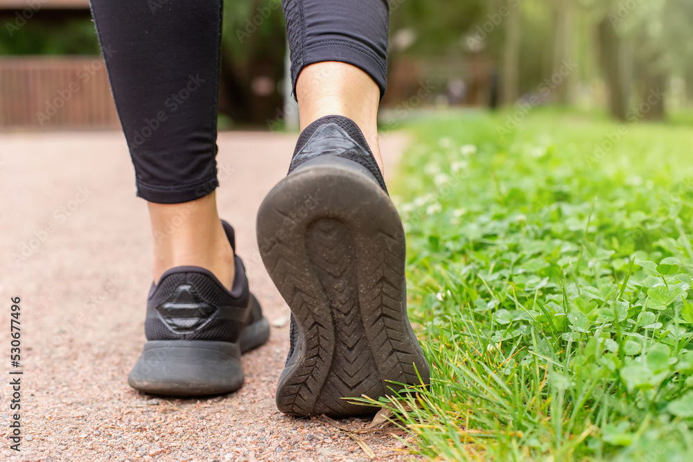a womans legs, in black sneakers , walking along a path made of small red stone